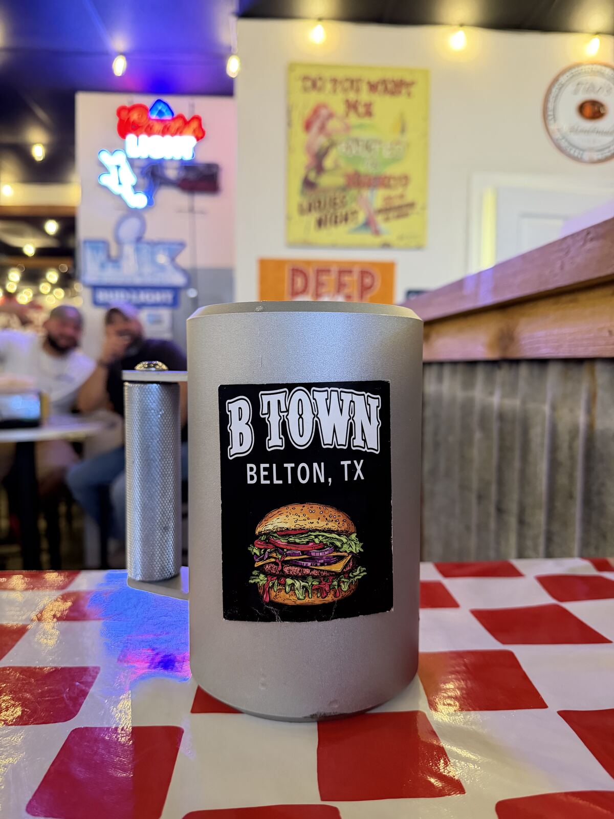 B Town Burgers cup on a checkered table with neon signs in the background